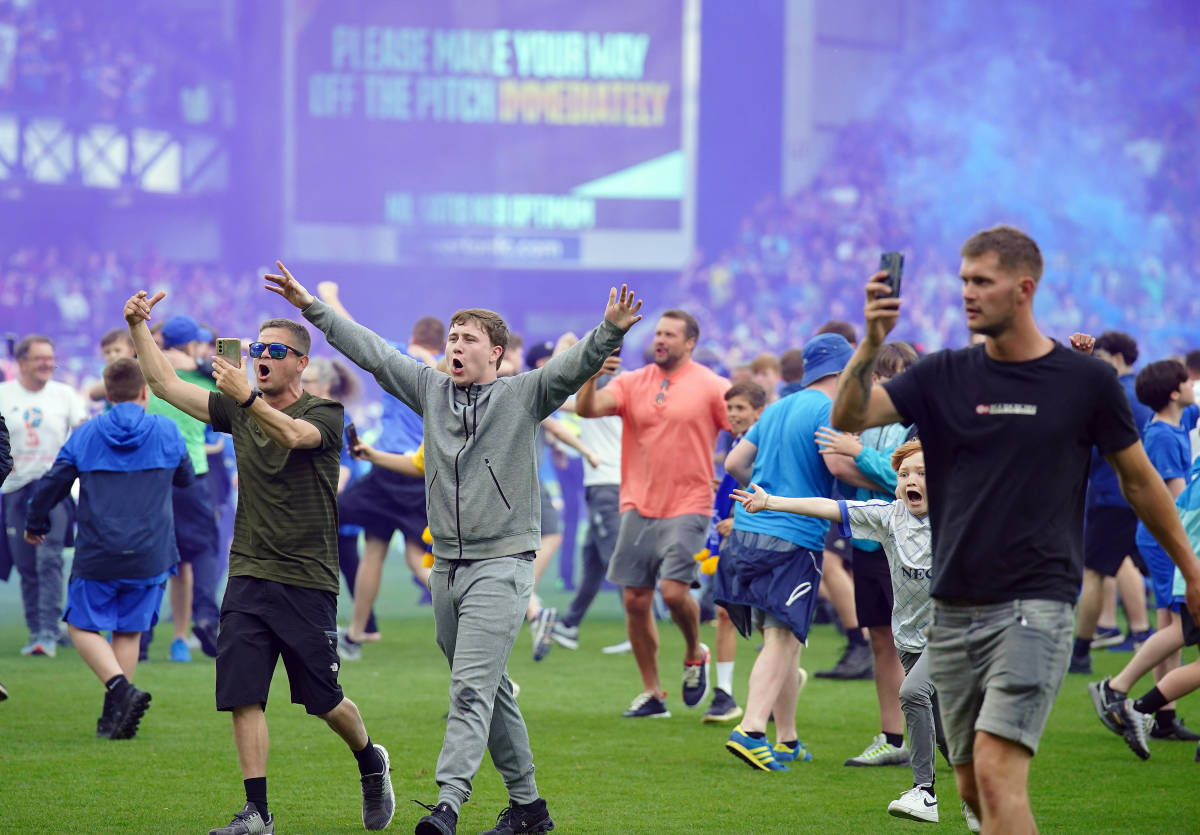 Everton fans pictured on the pitch at Goodison Park after watching their team beat Bournemouth 1-0 to avoid relegation from the Premier League in May 2023